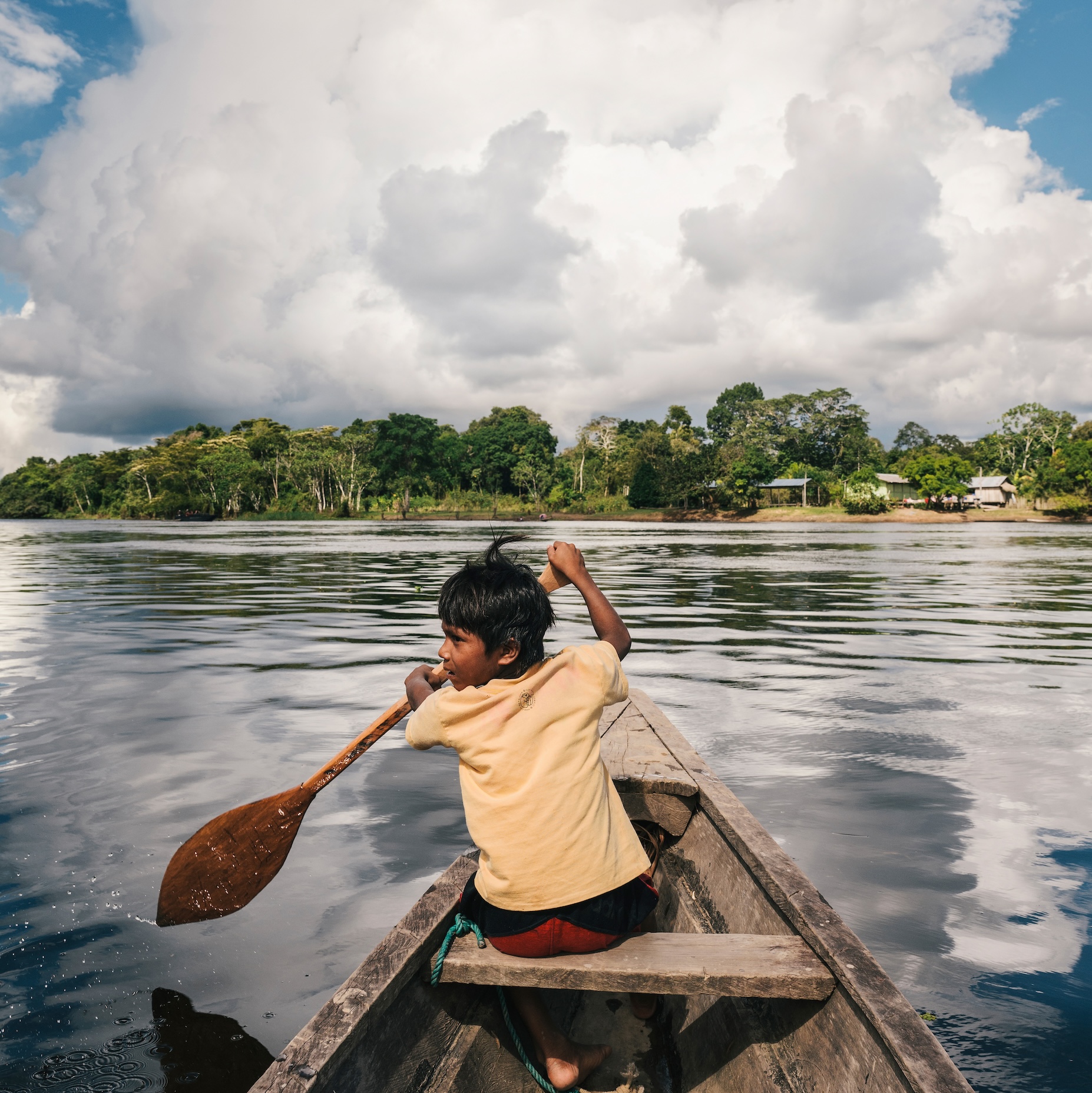 Boy paddling in boat in the water with clouds before him