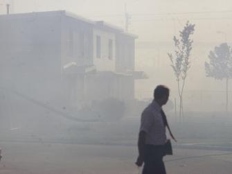 Smog clouds a city street, shrouding residential buildings and small trees as a person in a tie walks by.