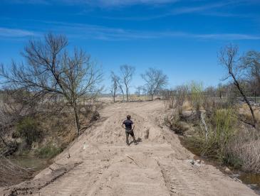 A man surveys water flow from a dusty road.